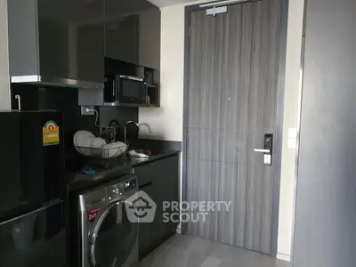 Modern kitchen with sleek black cabinets, washing machine, and microwave in compact layout.