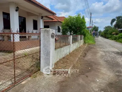 Charming suburban house with red-tiled roof and fenced yard on a quiet street.