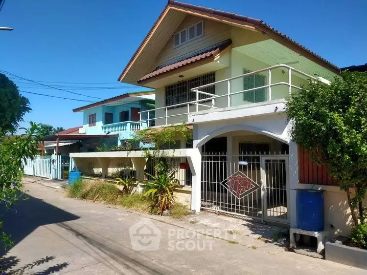 Charming two-story house with balcony and gated entrance in a serene neighborhood.