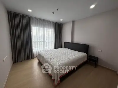 Spacious bedroom with large window and modern furnishings in a stylish apartment.