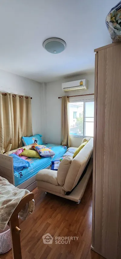 Cozy bedroom with wooden flooring and natural light, featuring a comfortable bed and sofa.