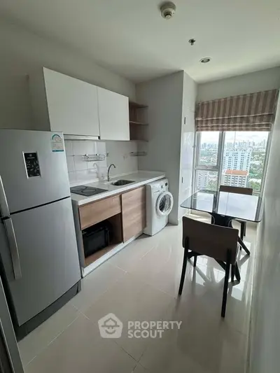 Modern compact kitchen with city view, featuring fridge, washing machine, and dining area.