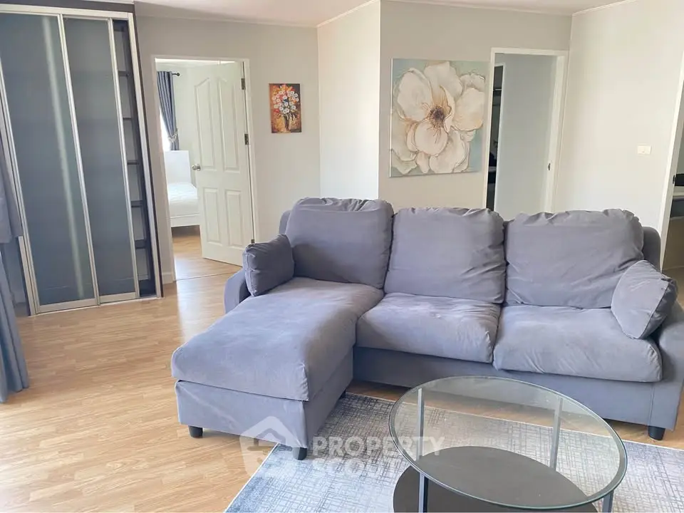 Spacious living room with modern gray sofa and glass coffee table, featuring elegant decor and wooden flooring.