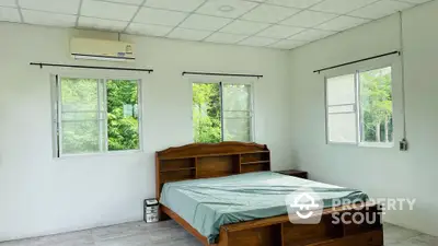 Spacious bedroom with large windows offering ample natural light, complemented by a sturdy wooden bed and a serene green view.