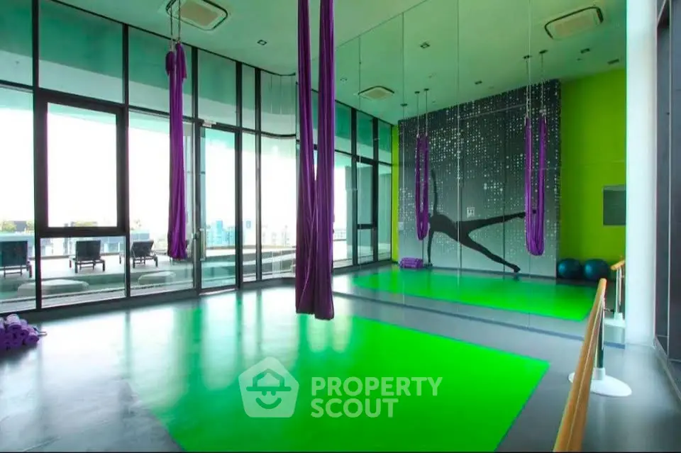 Modern gym with aerial yoga setup and vibrant green flooring in luxury building.