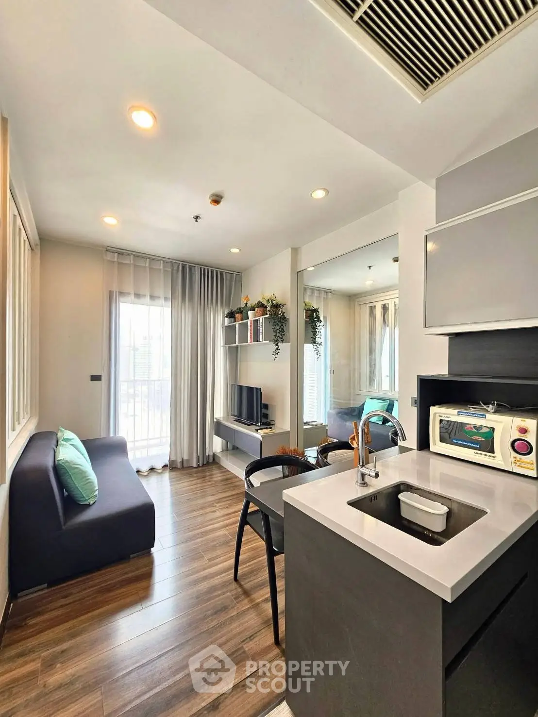 Modern open-layout living room with sleek kitchen and cozy seating area, featuring stylish decor and natural light.