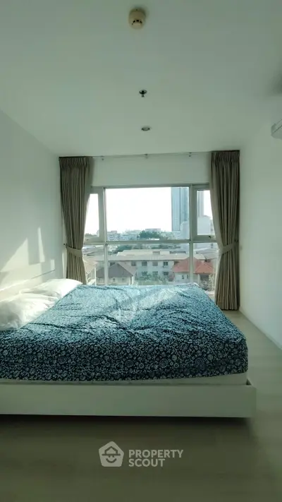 Bright bedroom with large window offering stunning city view, featuring a cozy bed and elegant curtains.