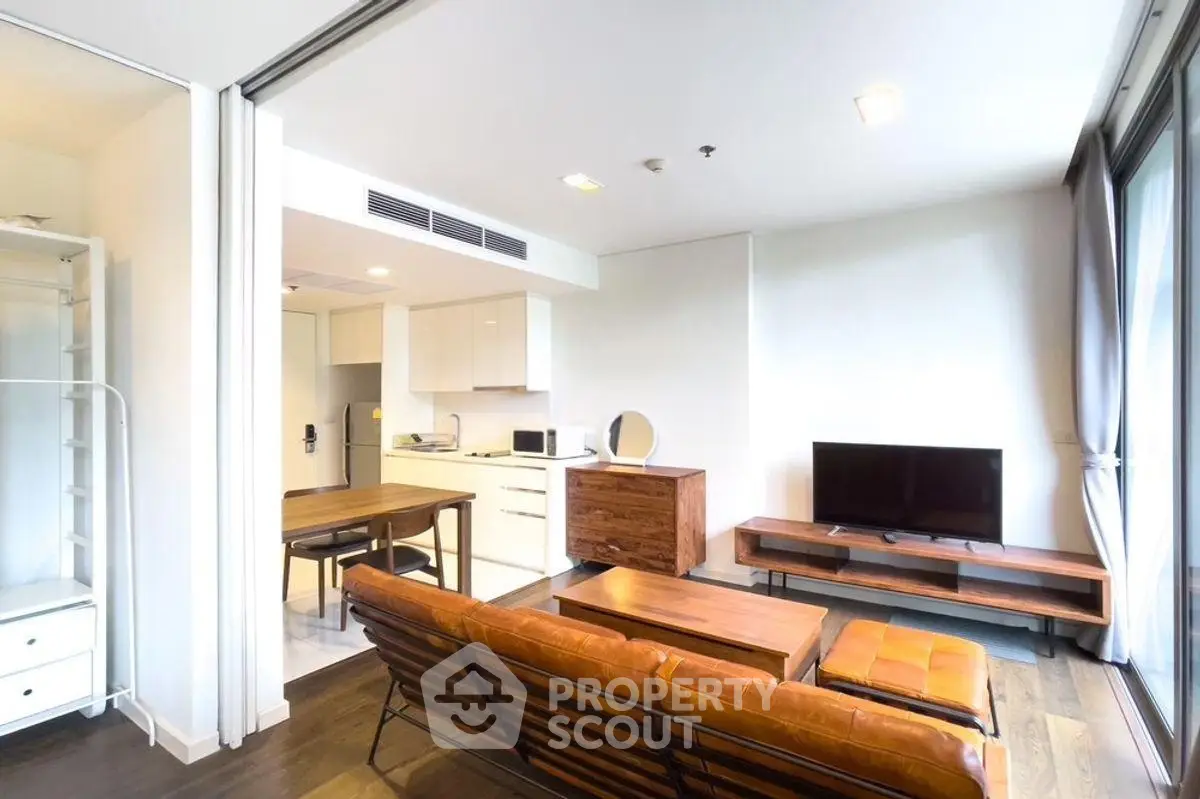 Modern open-plan living room with stylish furniture and kitchen area, featuring natural light and sleek design.