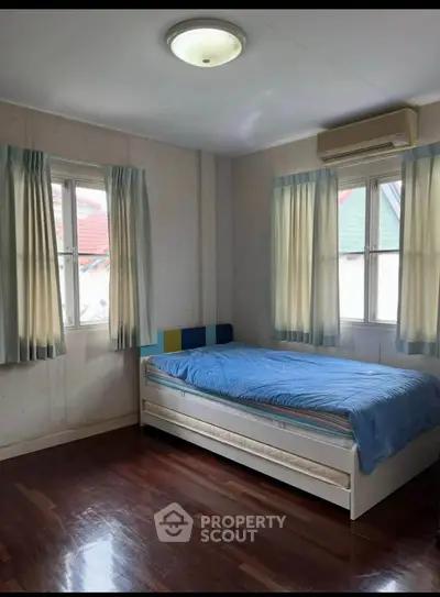 Cozy bedroom with wooden floors and natural light from multiple windows, featuring a single bed and air conditioning.