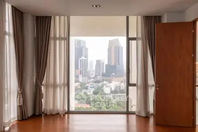 Spacious room with floor-to-ceiling windows offering stunning cityscape views, elegant curtains, and wooden flooring.