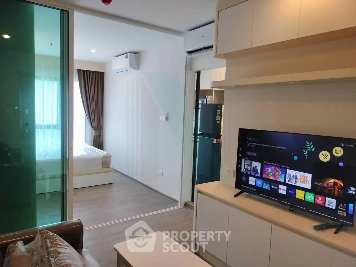 Modern apartment interior with open living room and bedroom, featuring sleek furniture and a smart TV.