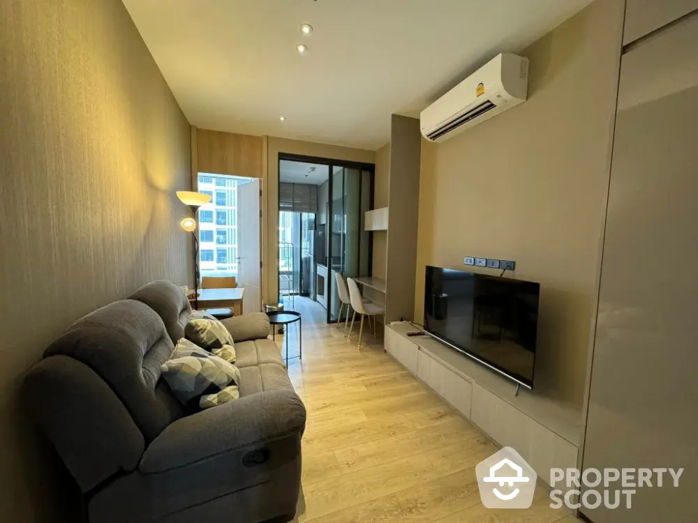 Modern living room with cozy sofa and TV, leading to a bright balcony view.