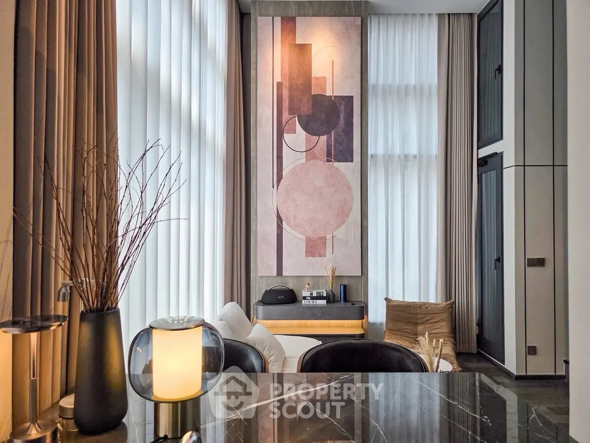 Modern living room with high ceilings and abstract art, featuring elegant decor and natural light.