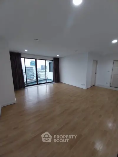 Spacious empty living room with wooden flooring and large windows offering city views.