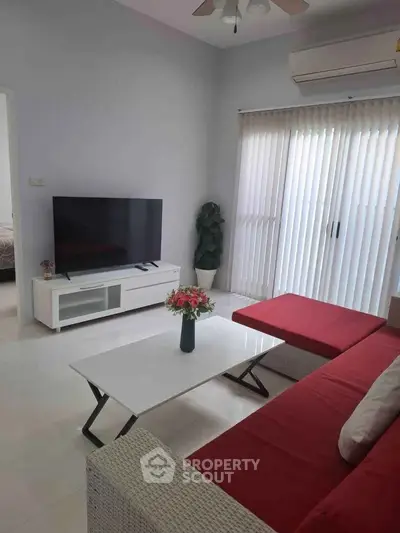 Modern living room with red sofa, flat-screen TV, and natural light from large window.