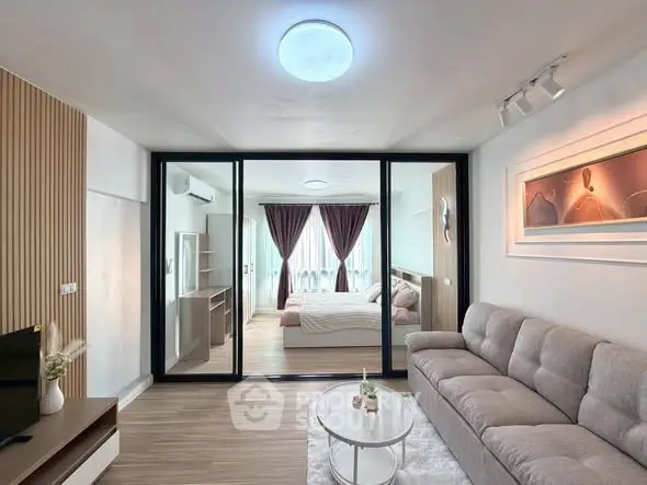 Modern living room with cozy sofa and glass partition leading to elegant bedroom.