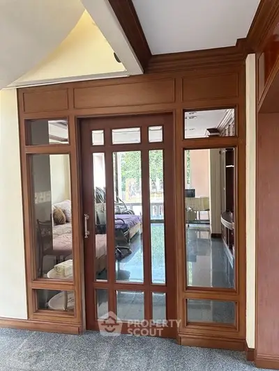 Elegant interior with wooden framed glass doors leading to a cozy bedroom, showcasing stylish design and natural light.