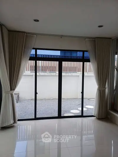 Spacious living room with large glass doors leading to a private outdoor area, featuring elegant curtains and glossy flooring.