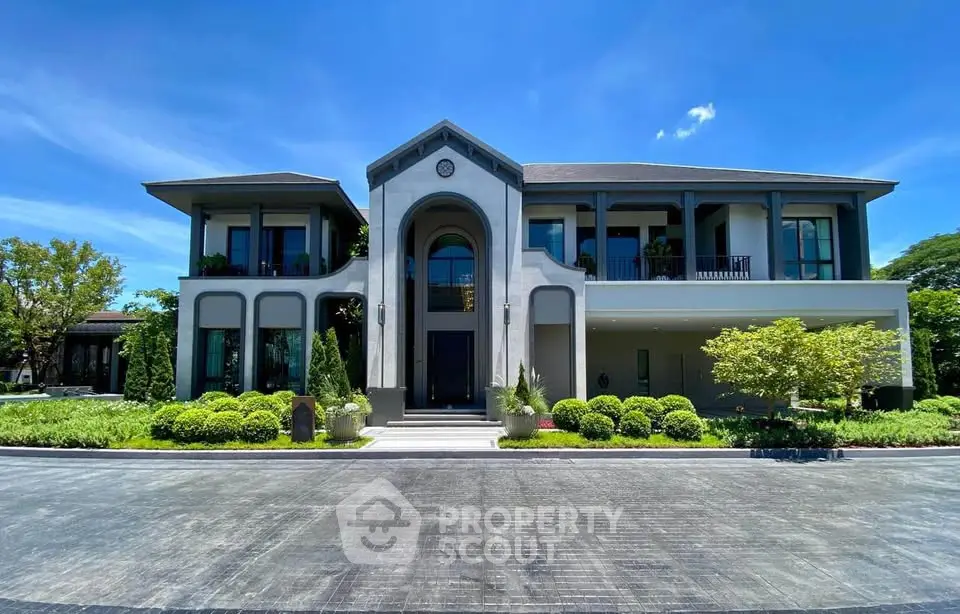 Luxurious modern mansion with grand entrance and lush landscaping under a clear blue sky.