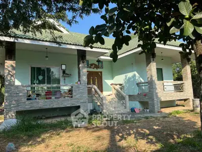 Charming single-story house with green roof and spacious front porch, surrounded by lush greenery.