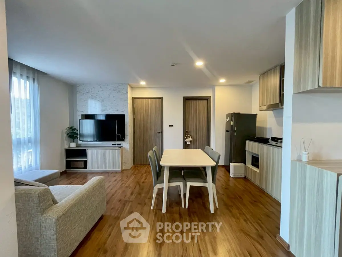 Modern open-plan living room with dining area and kitchen, featuring sleek furniture and natural light.
