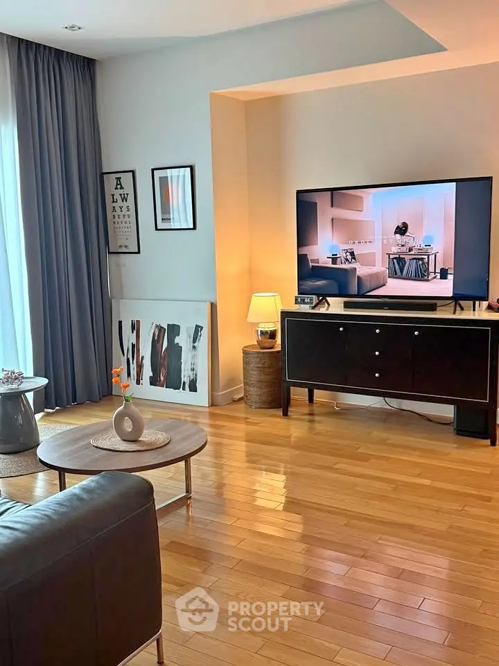 Stylish living room with modern decor and large TV, featuring wooden flooring and elegant curtains.