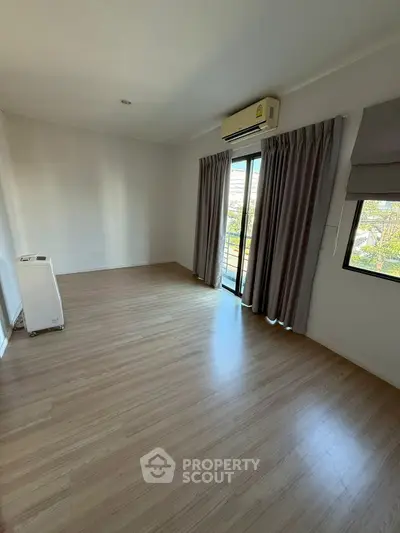 Spacious empty room with wooden flooring and balcony access, ideal for customization.