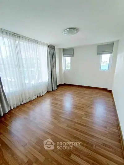 Spacious empty bedroom with wooden flooring and large windows for natural light.