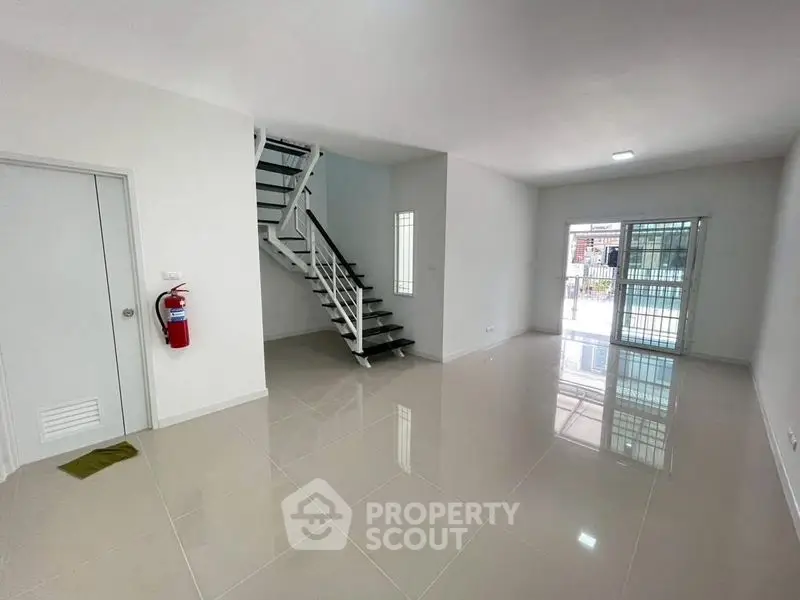 Spacious modern living room with sleek staircase and glossy tiled floors.