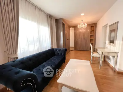 Elegant living room with plush navy sofa, chandelier, and wooden flooring.