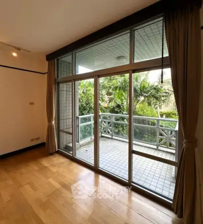 Spacious living room with large windows opening to a lush green balcony view.