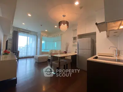 Modern open-layout living room with kitchen, featuring elegant chandelier and large windows for natural light.