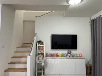 Modern living room with staircase, TV, and plush toys on a cabinet, offering a cozy family-friendly atmosphere.