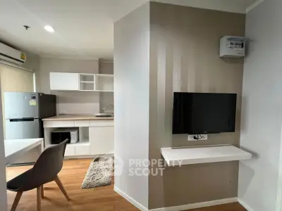 Modern apartment interior with sleek kitchen and cozy living area, featuring a wall-mounted TV and stylish furniture.