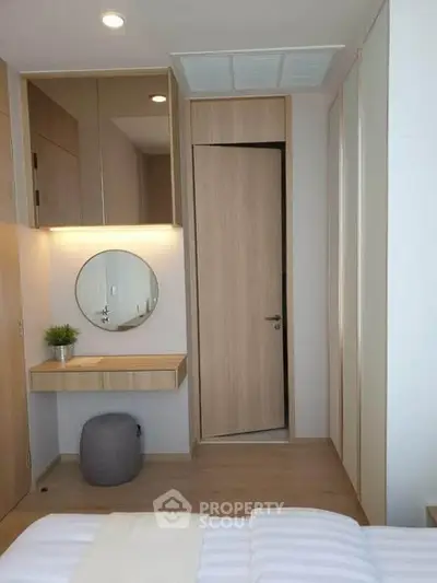 Modern bedroom with minimalist design, featuring a round mirror and wooden accents for a cozy ambiance.