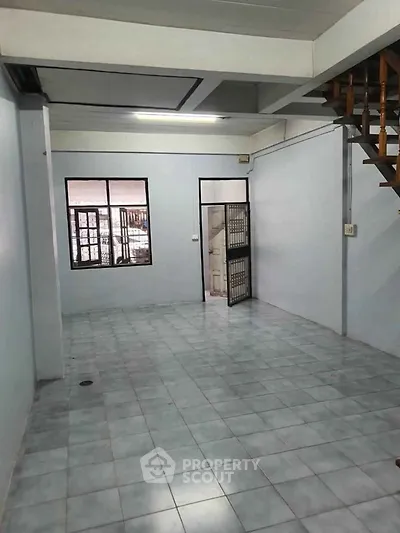 Spacious empty room with tiled flooring and staircase, ideal for customization.