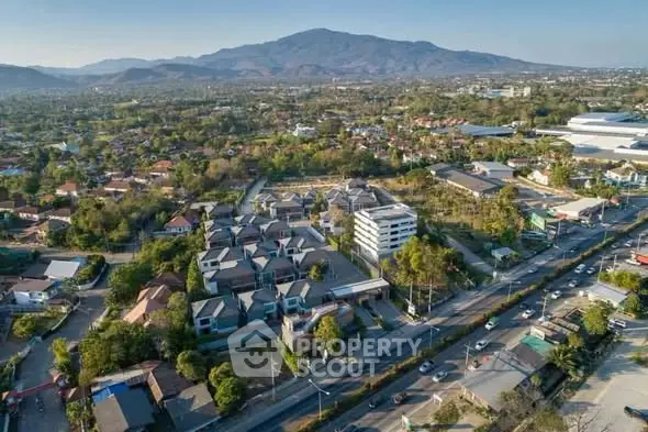 Aerial view of residential area with mountain backdrop, showcasing modern homes and lush greenery.