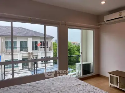 Bright bedroom with large windows and balcony access, offering a serene view of neighboring buildings.
