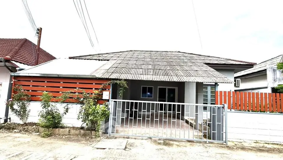 Charming single-story house with gated entrance and rustic roof in a serene neighborhood.