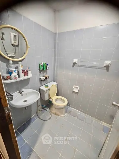 Compact bathroom with tiled walls, round mirror, and essential fixtures in a cozy real estate unit.