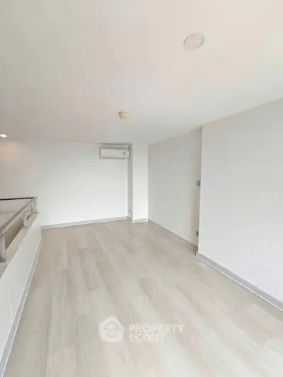 Spacious minimalist living room with light wood flooring and modern air conditioning unit.