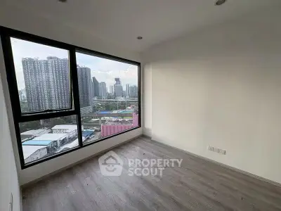 Spacious room with large window offering stunning cityscape views in modern high-rise building.