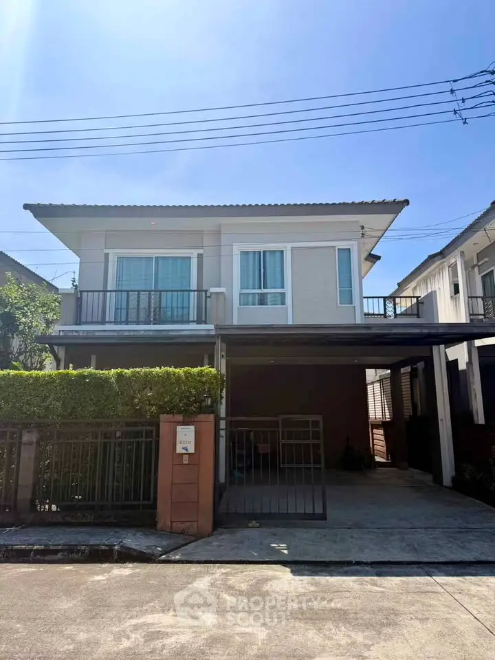 Modern two-story house with balcony and gated driveway in sunny neighborhood.