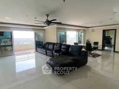 Spacious modern living room with leather sofa and dining area, featuring large windows and balcony access.