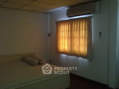 Cozy bedroom with ample natural light, featuring an air conditioning unit and warm-toned curtains, perfect for comfortable living.