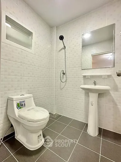 Modern bathroom with sleek fixtures and tiled walls, featuring a shower, toilet, and pedestal sink.