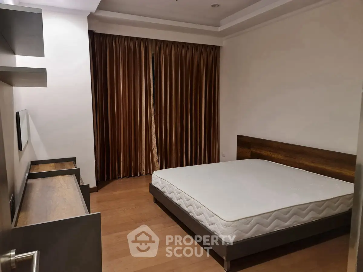 Spacious bedroom with wooden flooring and large window curtains