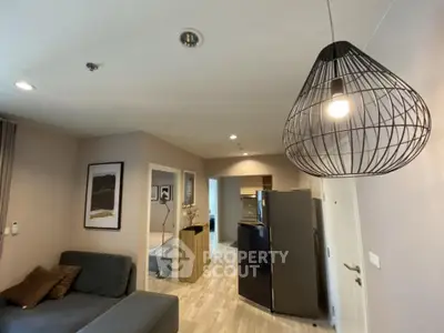 Modern living room with stylish lighting and open layout, featuring a cozy sofa and sleek kitchen area.