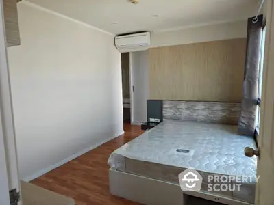 Modern bedroom with wooden flooring and natural light, featuring a comfortable bed and air conditioning.