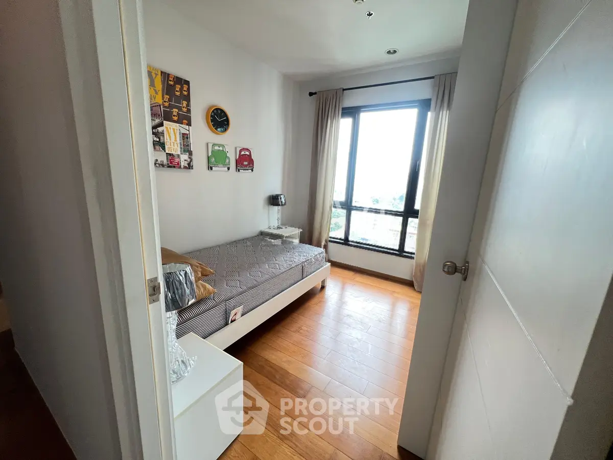 Cozy bedroom with wooden flooring and large window offering natural light and scenic views.